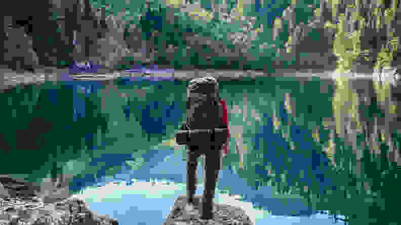 A man wearing a large hiking bag in front of a pond.