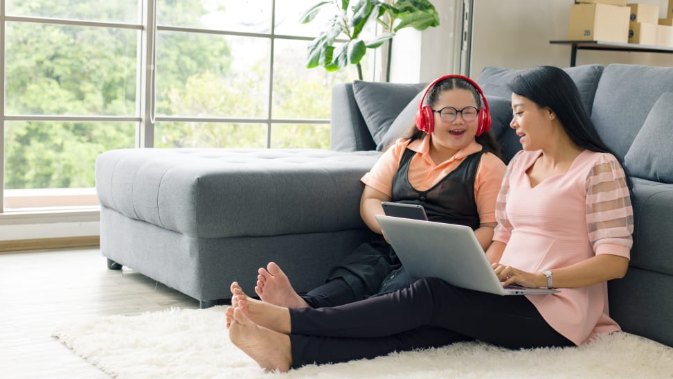 A mom and teenager daughter sit on the floor looking at a laptop