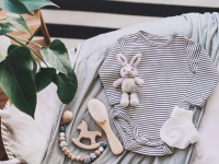 Still life background of cute baby products - changing basket with baby bodysuit, newborn clothes, knitted rabbit and wooden toy