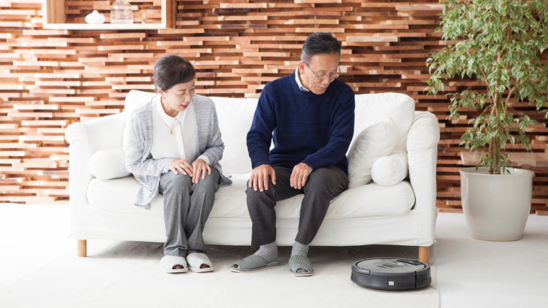 Two elderly people watching a robot vacuum