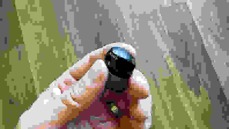 A hand holding one Sony WF-1000XM5 earbud in its fingers.