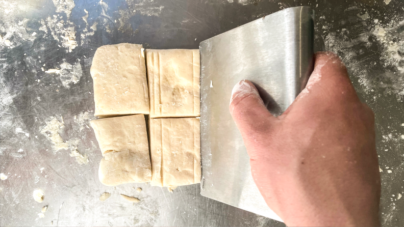 A person cutting square biscuits out of dough.