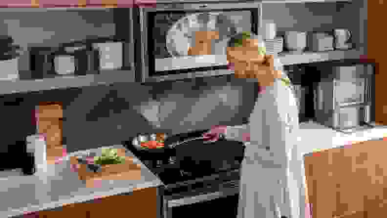 Person using skillet to cook vegetables on stovetop of the GE Café cooktop and range.