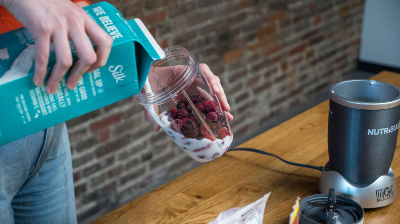 Our tester is pouring nut milk into the blending cup, making a smoothie with berries.