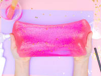 Hands stretching pink glitter slime with glue, mixing materials, and glitter in the background.