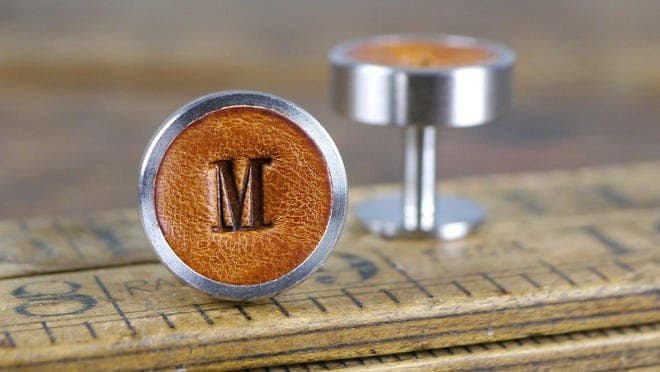 Leather cufflinks imprinted with the letter M.