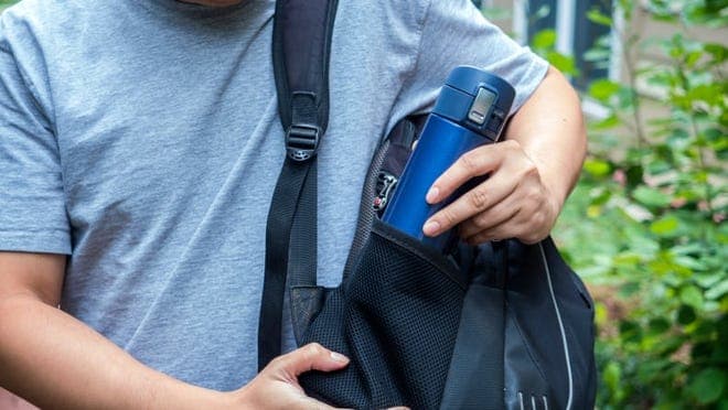 A person puts a stainless-steel travel mug in a backpack