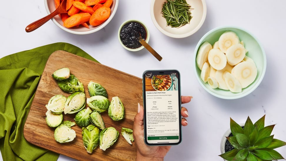 A countertop with healthy ingredients chopped, with a hand holding a phone that showcases a recipe