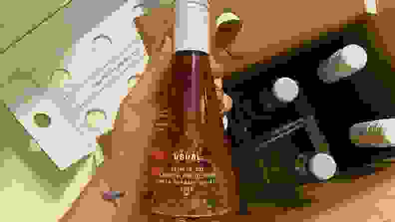 A hand holding a small Usual Wines bottle in front of the packaging.