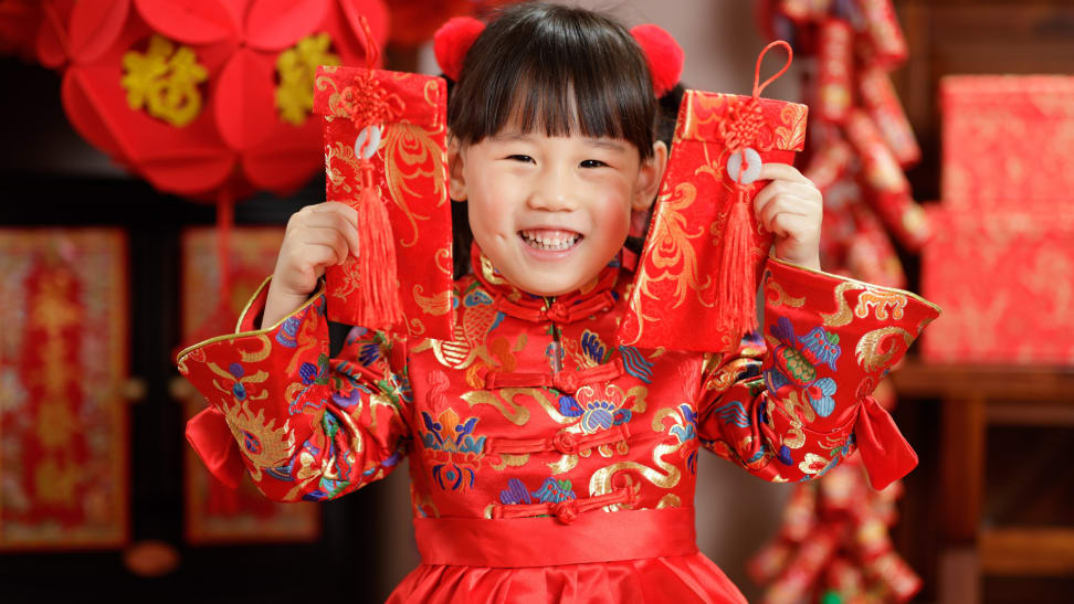 小女孩快乐地拿着两个红包,喜庆的春节装饰在她的身后。