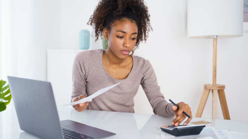 Person sitting at desk next to laptop while holding credit card and bill.