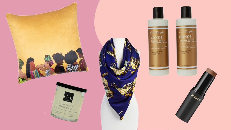 An image of several products on a pink background, including a yellow pillow, a candle, a scarf, haircare, and a foundation stick.