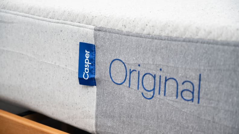 the foot of the casper mattress on a brown bed frame showing the tag and name embroidered on the bed