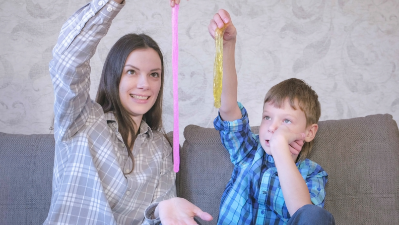 Smiling mom and son are playing with slime sitting on the sofa