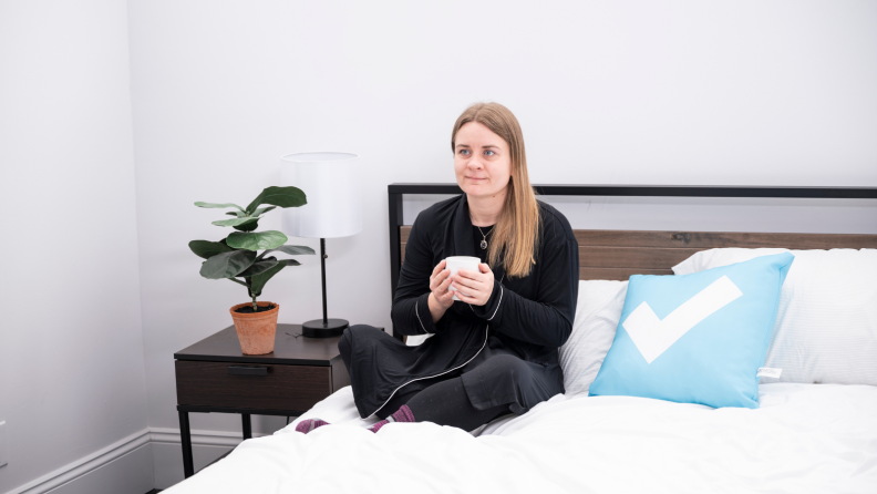 Girl sitting on a bed holding tea.