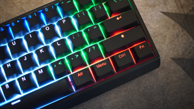 Close up angled shot of the Wooting 60he keyboard with rainbow backlit display turned on.