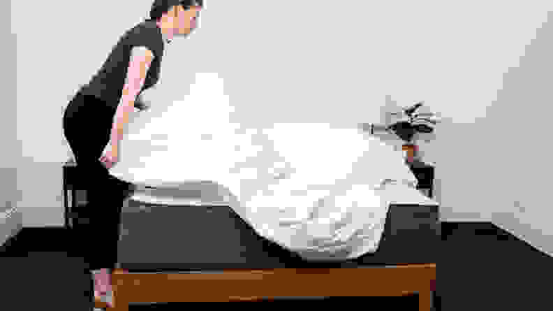 a woman spreads a sheet over the Casper Select mattress