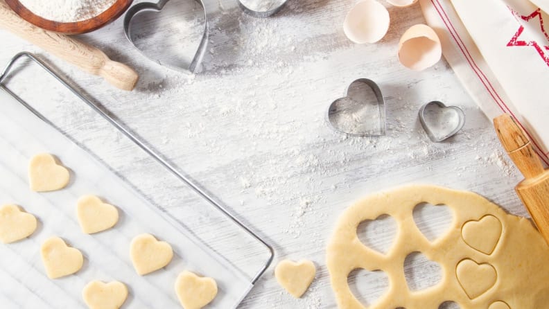 Cookie dough shaped into heart shapes with stencils and other baking tools on marble countertop