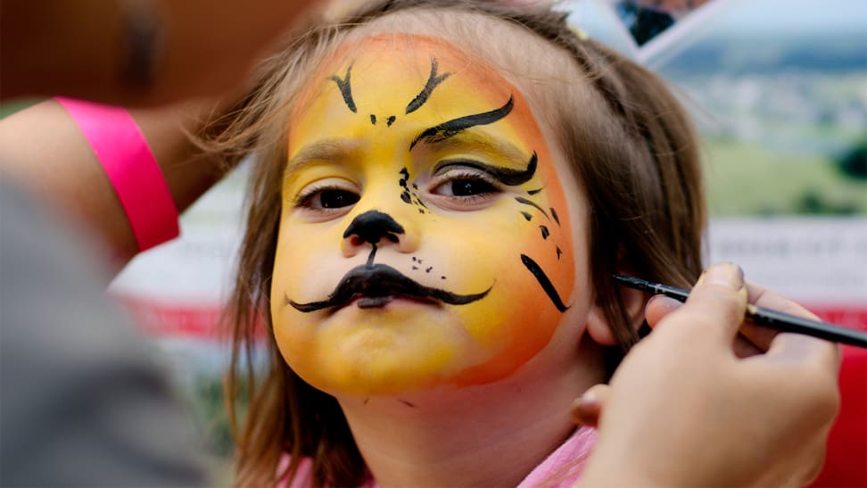 A child getting her face painted to look like a lion for Halloween.