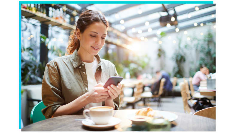 Person sitting at restaurant checking phone in front of cup of coffee.