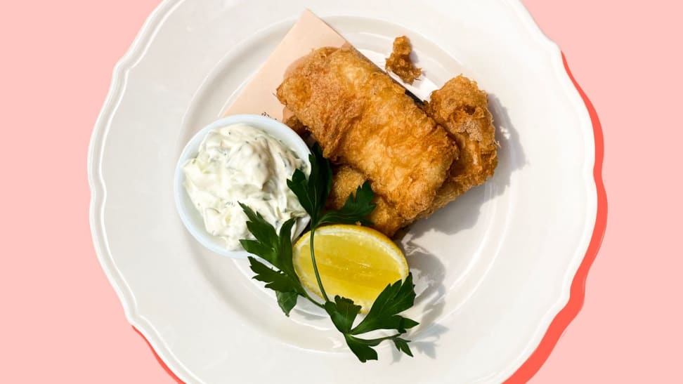 Beer-battered fried fish on a white plate accompanied by homemade tartar sauce and a lemon wedge.