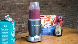 A Nutribullet personal blender filled with a berry smoothie sits on a counter next to its ingredients.