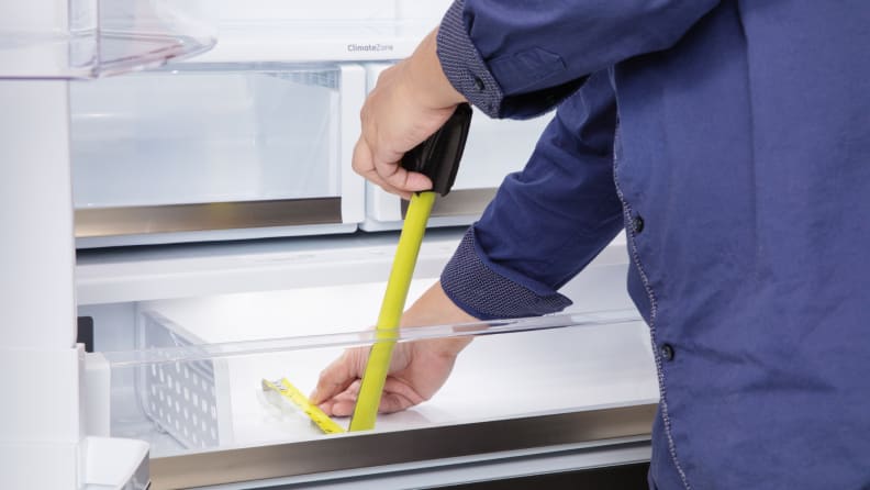 A person measures a refrigerator drawer with a measuring tape
