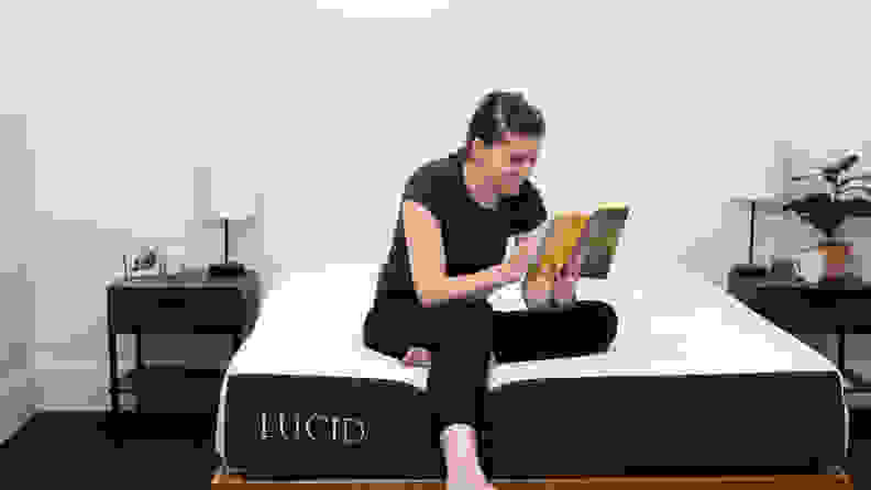 a person sits on the edge of the lucid mattress reading