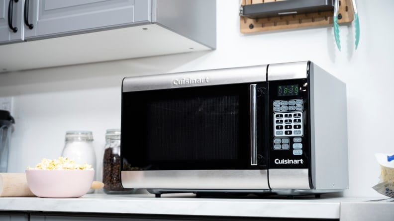 A microwave on a kitchen counter next to a bowl of popcorn.