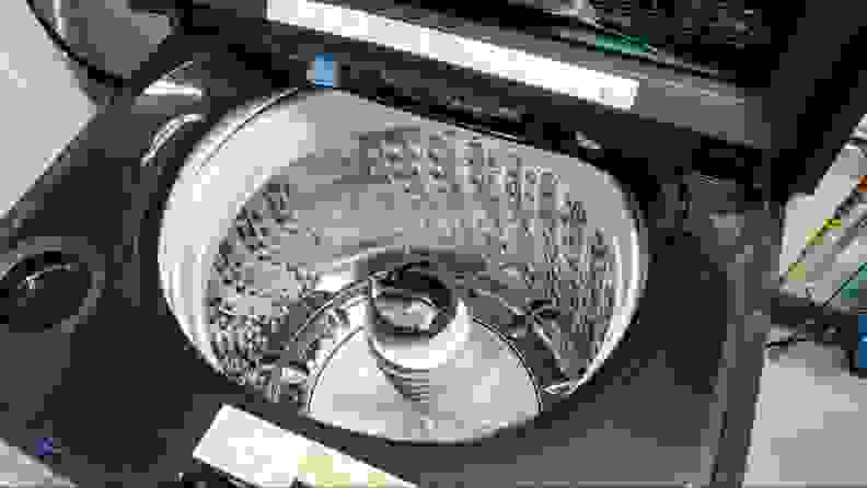 The silver inside of a black washing machine with agitator pole, showing a white garment inside.
