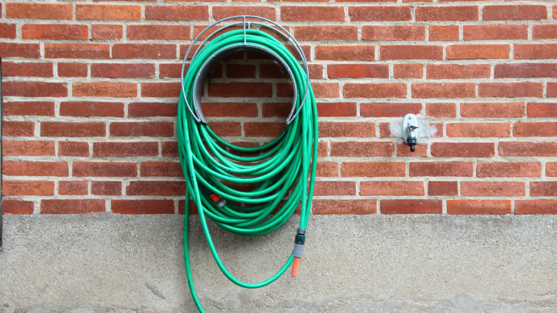 Unattached garden hose hanging up on side of a brick wall