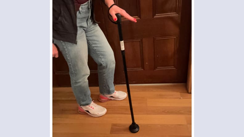 Person standing next to the Kmina Folding Orthopedic Cane while resting hand on top of handle.