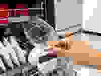 A hand holding up a dry, spotless glass in front of a Bosch dishwasher