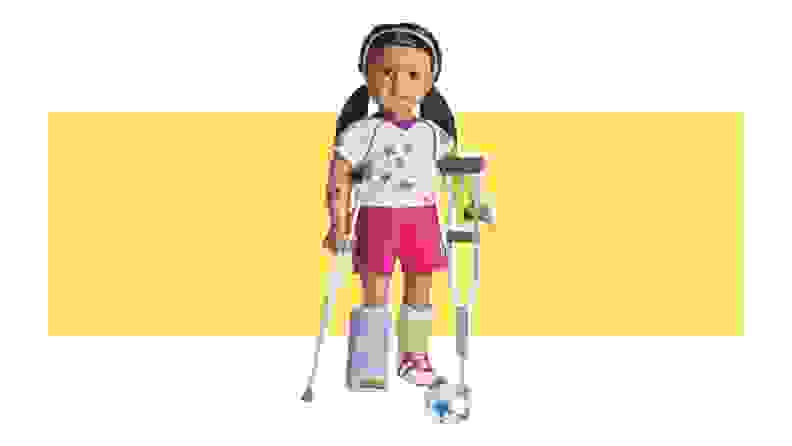 An American Girl doll with wearing athletic attire, with a purple foot cast on, and holding onto crutches.