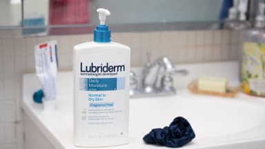 A large bottle of body lotion standing on the side of a sink.