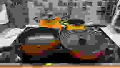 Orange, red, yellow Meyer skillets and pots sitting on top of cooktop in kitchen.