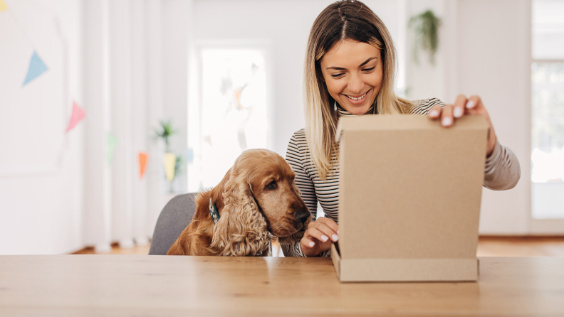 Woman opening cardboard box package with her dog sitting next to her