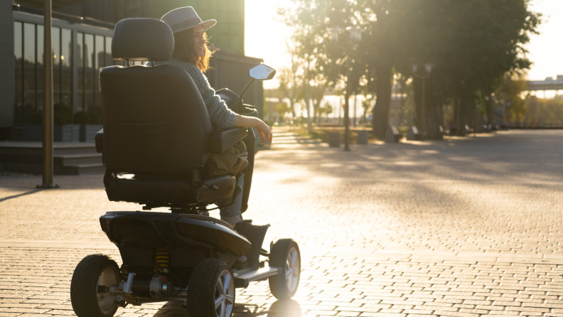 A person in an electric wheelchair drives on a cobblestone road at dusk