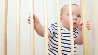 Toddler gripping the bars of a protective gate.