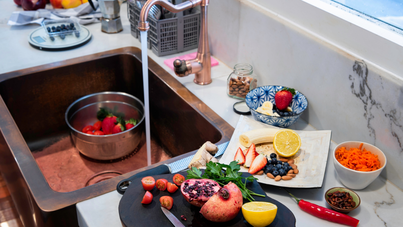 Fruits and vegetables sitting on cutting board next to copper sink.