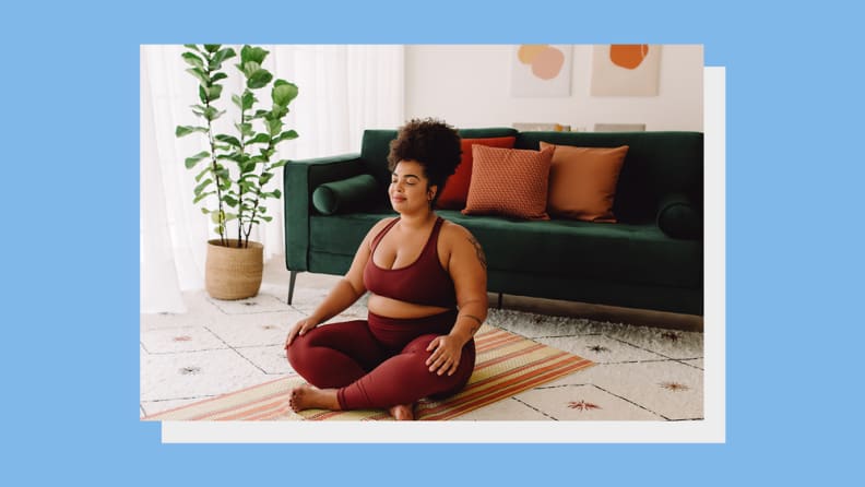 Person with curly hair sitting on yoga mat and meditating with eyes closed.