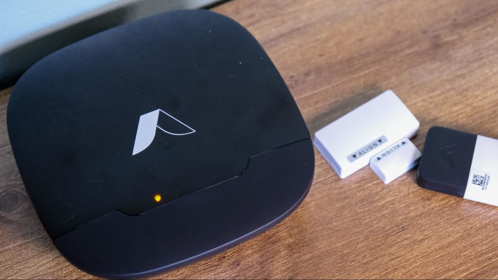 The Abode Security Kit security base, window/door sensor, and key fob sitting on a wood table.