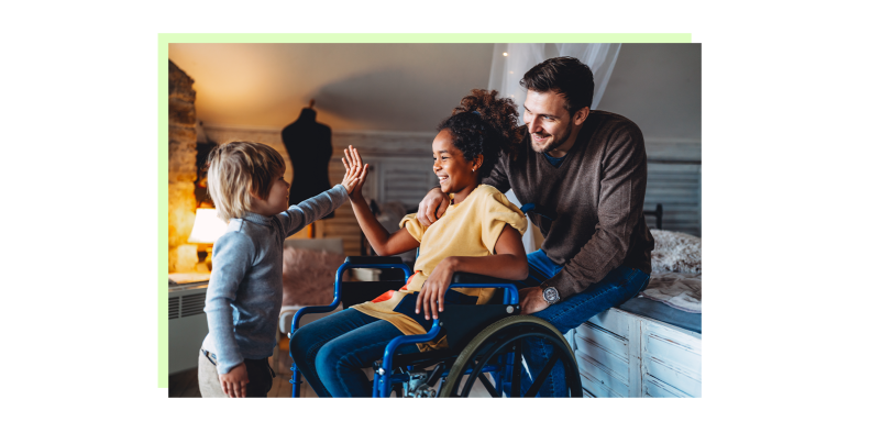 A child high-fiving a special needs child in a wheelchair with an adult behind.