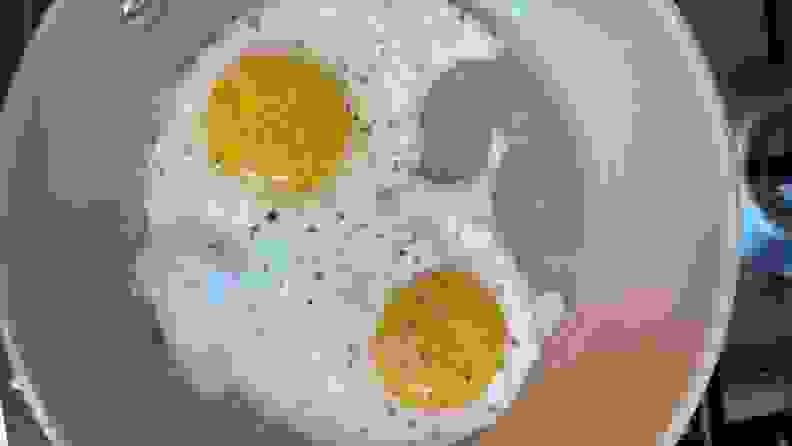 Two seasoned eggs being fried inside of nonstick skillet pan.