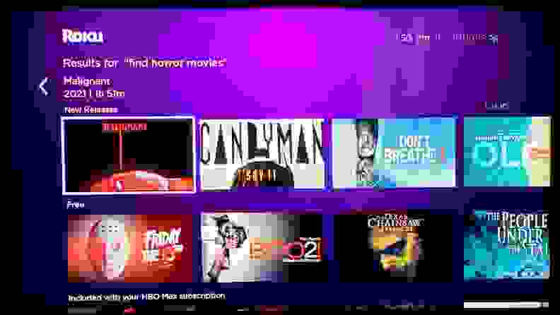 The Roku menu is shown on TV screen, with multiple streaming app squares against a purple background, with horror movies called up via voice search.