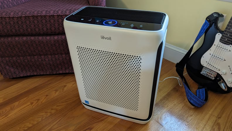 A Levoit Vital 200S air purifier in white and black sits on the floor next to a guitar.