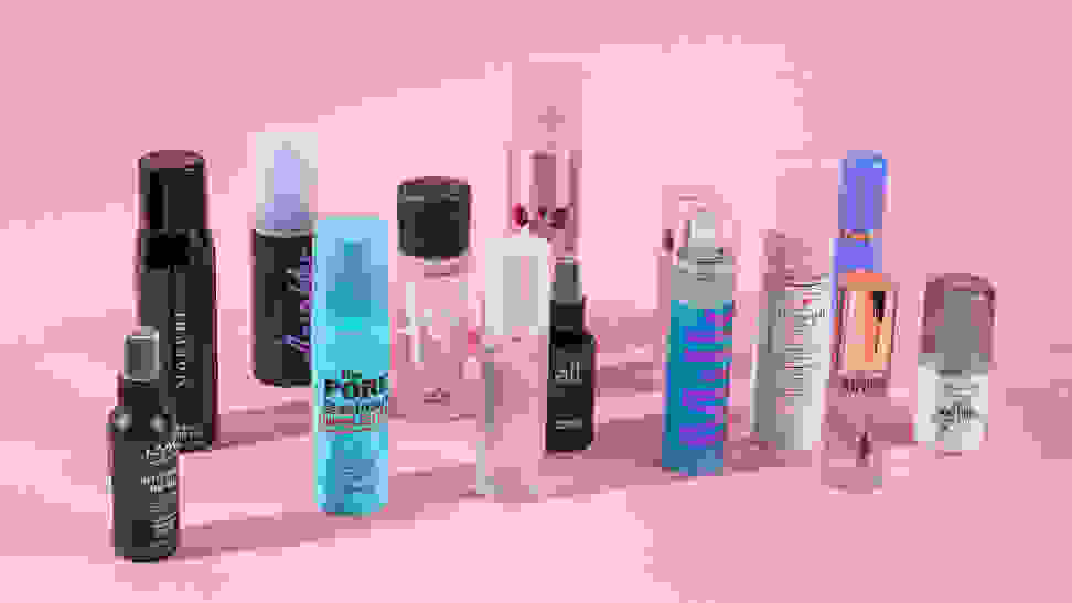 A bunch of makeup setting sprays standing on a pink background.