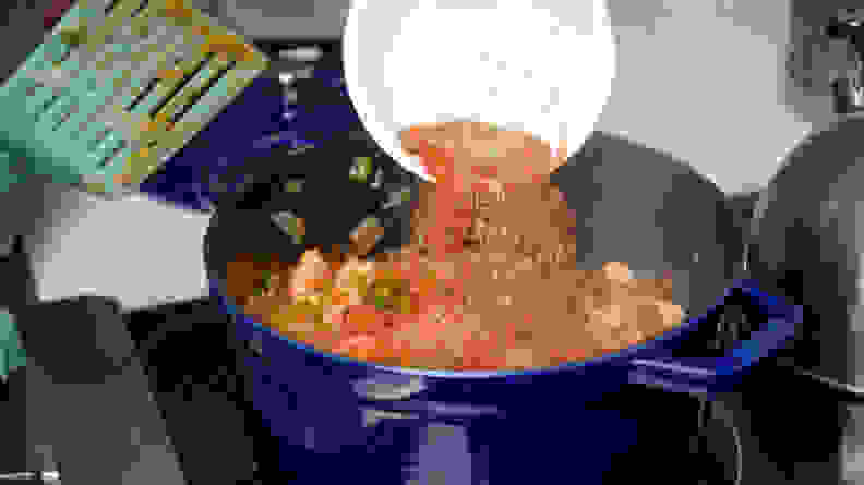 A bowl of spices and herbs being poured into a big pot of jambalaya cooking on a stove.