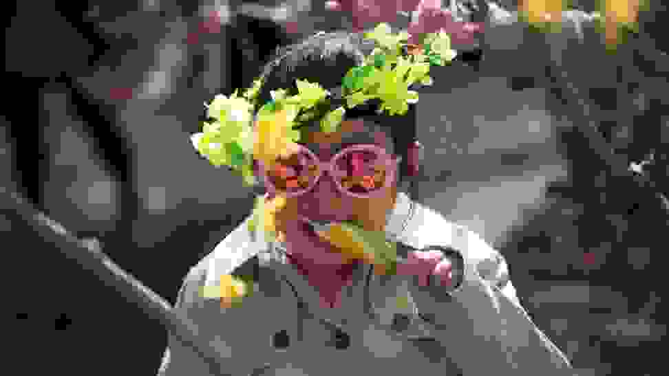 A child in pink sunglasses and a headpiece with yellow flowers enjoys a popsicle in the sun.