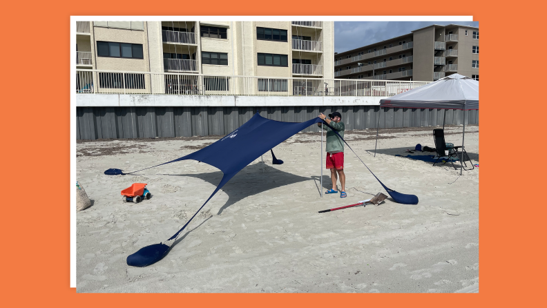 Person setting up beach canopy on sand.